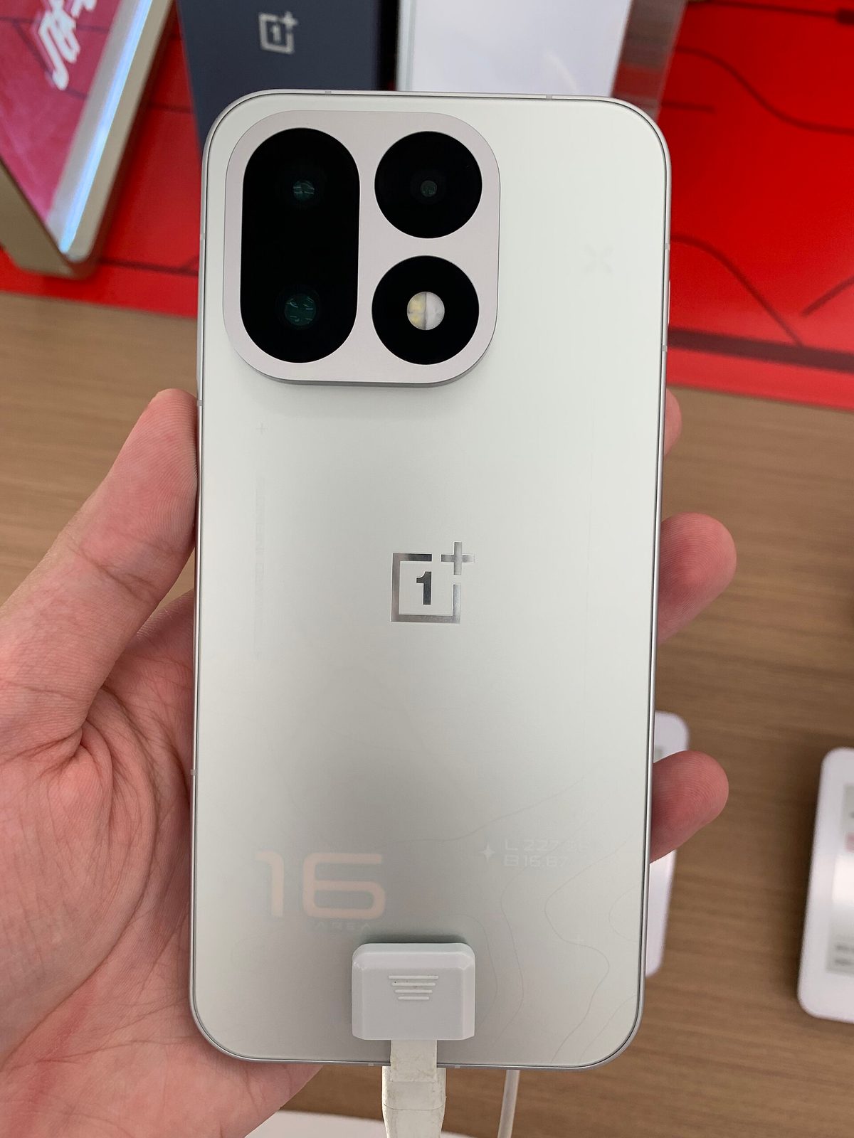 OnePlus 16 in hand, rear view showing the camera module and the "16" engraving, photographed at a China retail launch