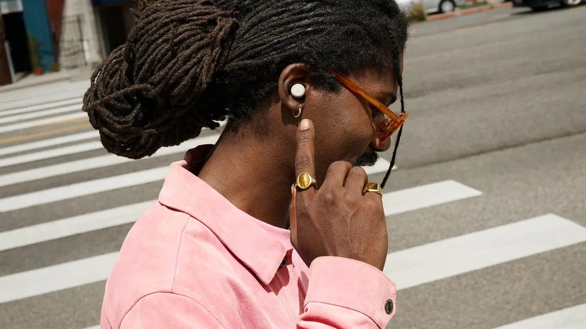 Person wearing a white Google Pixel Buds Pro 2 earbud, touching it with a finger while crossing a street