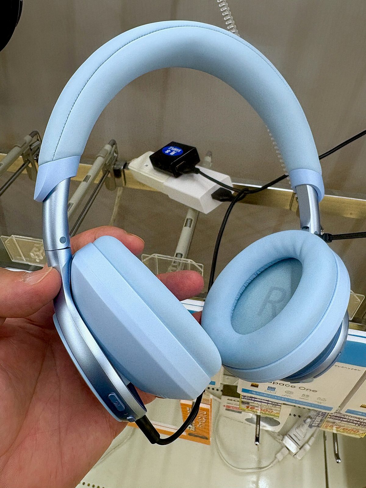 Soundcore Space One headphones in light blue, held in hand at a store display